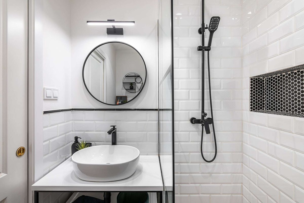 A modern white bathroom with subway tiles, a round black-framed mirror, a bowl basin on a white vanity and a glass shower with black fittings
