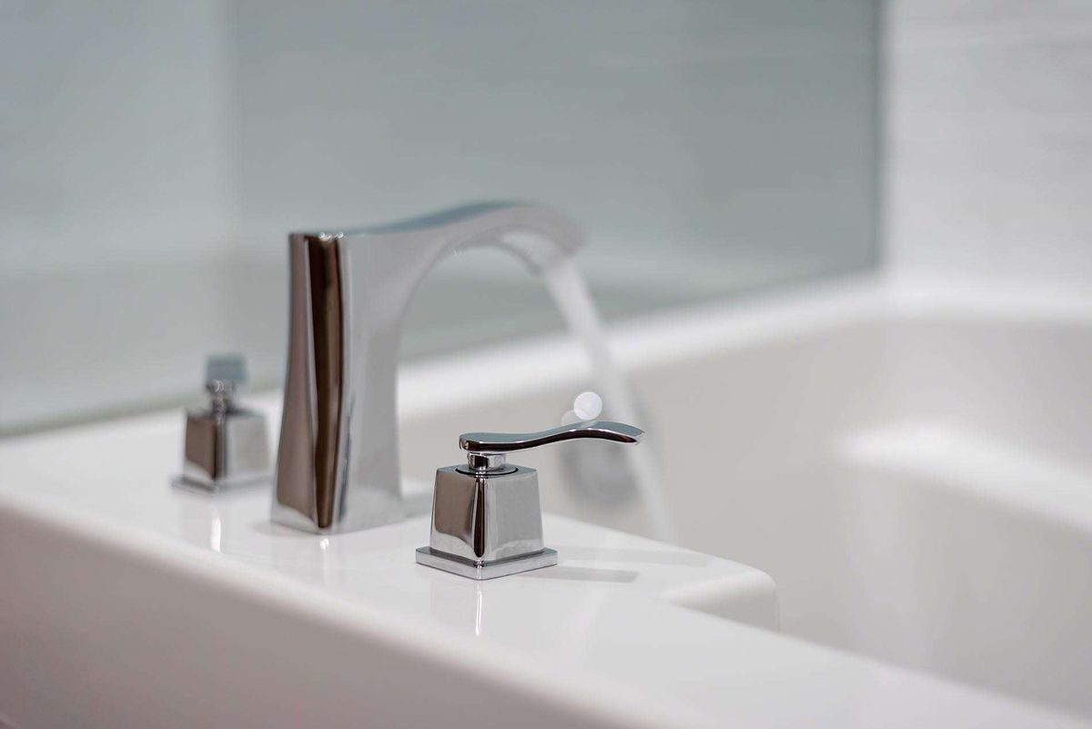 Close view of a chrome tap with square handles running water into a white bath